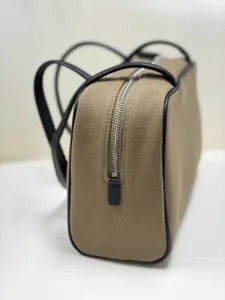 Minimalist canvas shoulder bag with black leather trim, top zipper, and dual handles.