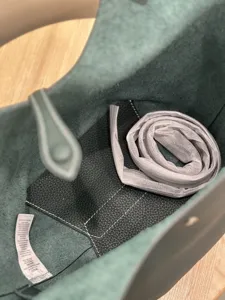 Interior detail of green leather bucket bag showing black inner pocket and rolled shoulder strap.