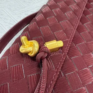 Burgundy woven leather handbag detail shot featuring stylish gold knot hardware and latch.