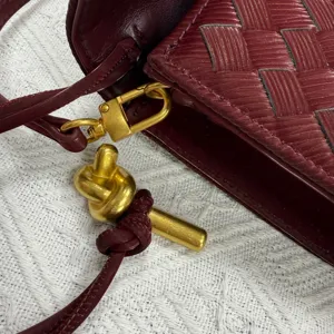 Burgundy woven leather bag close-up, showing gold tone knot hardware and fine detail craftsmanship.