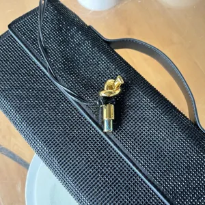 Détail du sac de soirée noir en strass étincelant avec fermoir noué doré élégant.