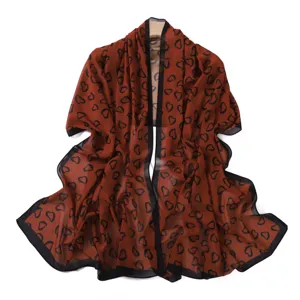 Dettaglio ravvicinato della sciarpa in chiffon con stampa di cuori neri su tessuto marrone.