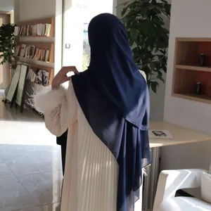 Elegant chiffon hijab and pleated dress detail with feather cuffs in indoor setting.