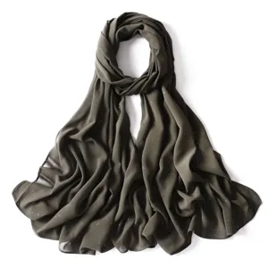 Primo piano di sciarpa in chiffon verde scuro con riflessi dorati, drappeggio leggero.