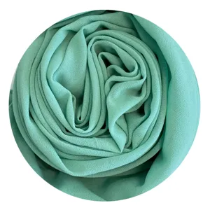 Close up view of soft mint green chiffon hijab fabric texture rolled in circular shape.