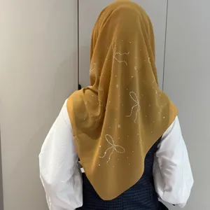 Vue détaillée du foulard en mousseline moutarde avec motifs de nœuds en strass brillants.
