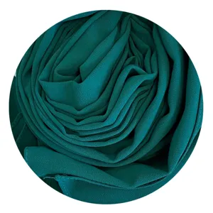 Detail shot of rolled dark green chiffon hijab headscarf showing fine fabric texture.