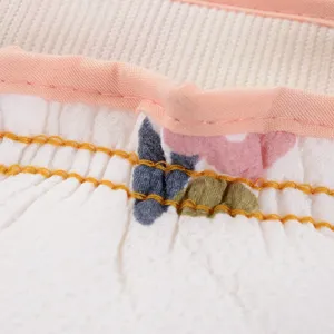 Close-up detail of soft textured bath exfoliating mitt with pink binding and yellow stitching.