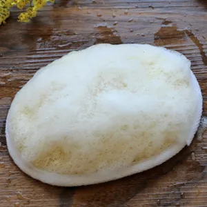 Natural loofah bath sponge with rich foam on wet wooden table for daily body exfoliation.