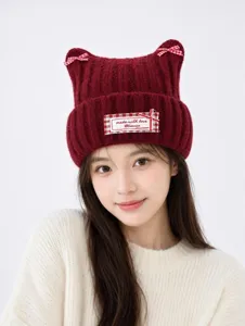 Detail view of dark red knitted cat ear hat with checkered bows and a woven label.