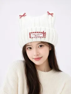 Close-up detail of a cute white knitted cat ear hat with red plaid bows and a cute woven label.