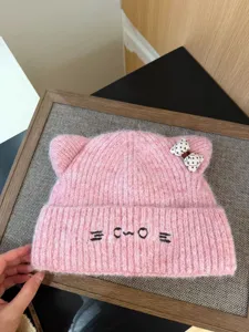 Primer plano detallado de un gorro de punto rosa con orejas de gato, bordados y un lazo.