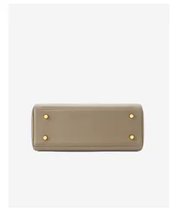 Gedetailleerd opname van de leren handtasbodem met beschermende metalen voetjes in taupe.