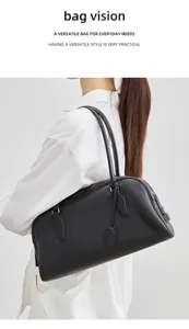 Detail view of minimal black leather boston bag on model, showing pebbled texture and handles.
