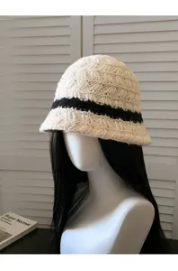 Detail du bob en tricot presentant la texture creme douce et la bande noire elegante.