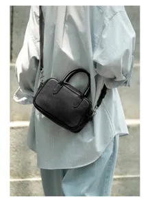 Detail shot of a black genuine leather Boston bag worn crossbody, showing texture and strap.