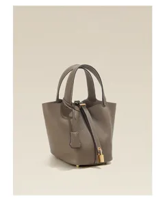 Detailed view of the elegant taupe leather bucket handbag with gold padlock and dual top handles.