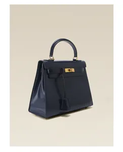 Détail de sac à main en cuir bleu foncé verni, forme trapèze, serrure en métal et poignée.