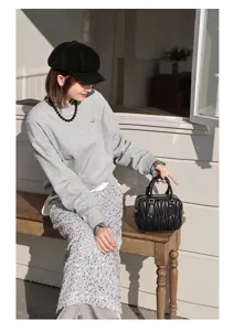 Outdoor detail shot of a black pleated leather mini bowling bag held by a fashion model on a bench.