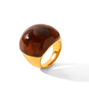 Gros plan detail de bague en acier inoxydable dore avec grande pierre resine dôme marron.