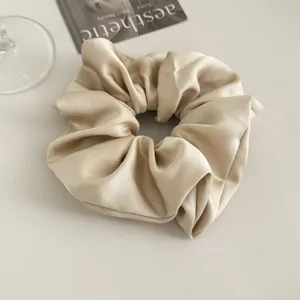 Elegant champagne satin hair scrunchie detail view, soft shiny fabric ponytail holder.