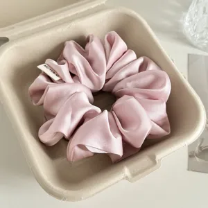 Nahaufnahme eines weichen rosa Satin-Haargummis, platziert in einer schicken Pappschachtel.