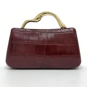 Vista detallada del bolso burdeos con textura de cocodrilo y elegante asa dorada.