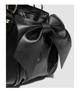 Schwarze Falten-Damentasche Detail mit eleganter Schleife und goldenen Metallringen.