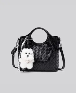 Detailansicht der schwarzen geflochtenen Ledertasche mit flauschigem Welpen-Plüsch-Anhänger.
