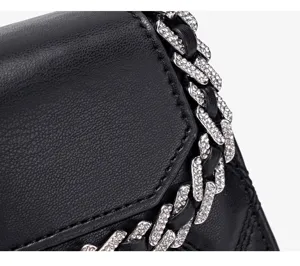 Detailopname van een zwarte lederen handtas met schitterende strass ketting en klepdesign.