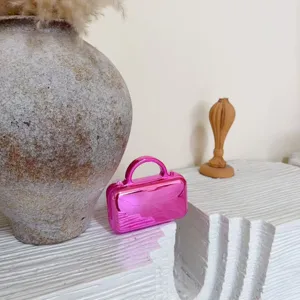 Detailed shot of a shiny pink metallic mini handbag on a sculptural white display stand.
