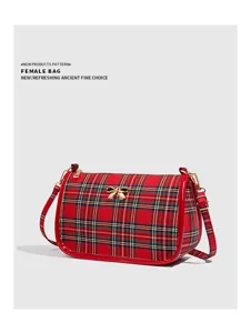 Vue détaillée du sac à bandoulière à carreaux rouges, avec bordure brillante et nœud doré.