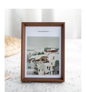 Wooden photo frame detail with retro winter snow landscape art print display tabletop.