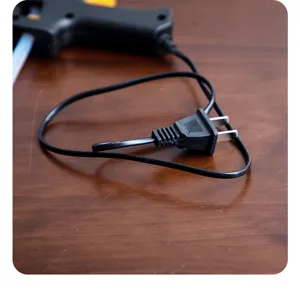 Close-up detail of the black power plug and cord of a hot melt glue gun on a wooden surface.