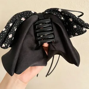 Schwarze florale Schleifen-Haarklammer Detail, elegante Satin-Textur und stabiler Kunststoffgreifer.