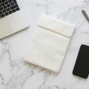 Detail view of white waterproof laptop sleeve on marble desktop with accessories.