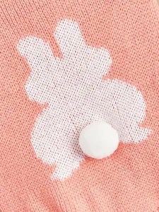 Close-up of pink knit pet sweater detail with cute rabbit pattern and fluffy pom-pom tail.
