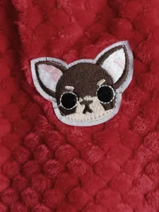 Detailed view of cute cartoon dog head embroidery patch on soft red coral fleece pet clothing.