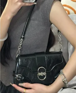 Detailed shot of a black glossy baguette shoulder bag with silver hardware and chain strap.
