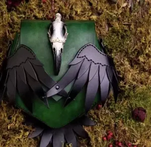 Dunkle gothische Rabenschädel Umhängetasche mit schwarzen Lederflügeln und grünem Lederdetail.