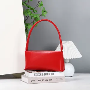 Red leather shoulder bag detail, stylish baguette handbag on decorative books in clean studio.