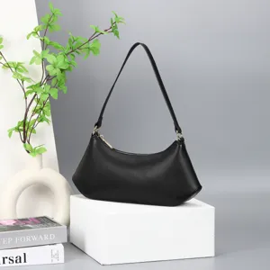 Detail view of a sleek black shoulder bag on a white display stand with green leaf props.