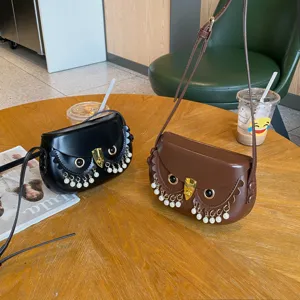Detailaufnahme der Eulen-Satteltasche mit Perlenquasten und Metallverschluss auf Holztisch.