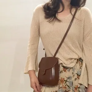 Detailansicht der braunen Retro-Umhängetasche getragen mit lässigem Beigen Strickoberteil.
