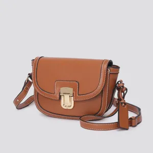 Brown leather saddle bag close-up showing white contrast stitching and metallic gold lock detail.