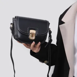 Close-up detail of black leather saddle bag with white contrast stitching and golden clasp.
