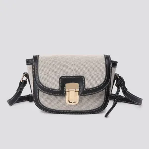 Color-block saddle bag detail showing premium canvas texture, black leather trim and gold clasp.