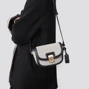Detailed view of canvas contrast saddle bag, shoulder strap, gold lock, fine stitching.