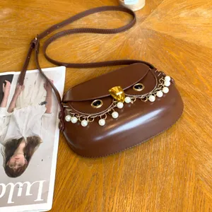 Nahaufnahme der braunen Eulen-Satteltasche mit Perlenkette und Metallverschluss am Tisch.