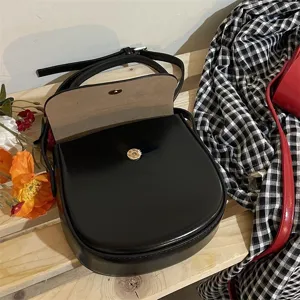 Schwarze Ledertasche Detail mit glatter Textur, minimalistischer Klappe und goldener Hardware.